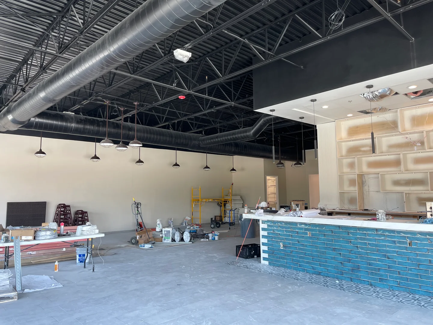 Bright commercial interior under construction with exposed round ductwork above the ceiling line.