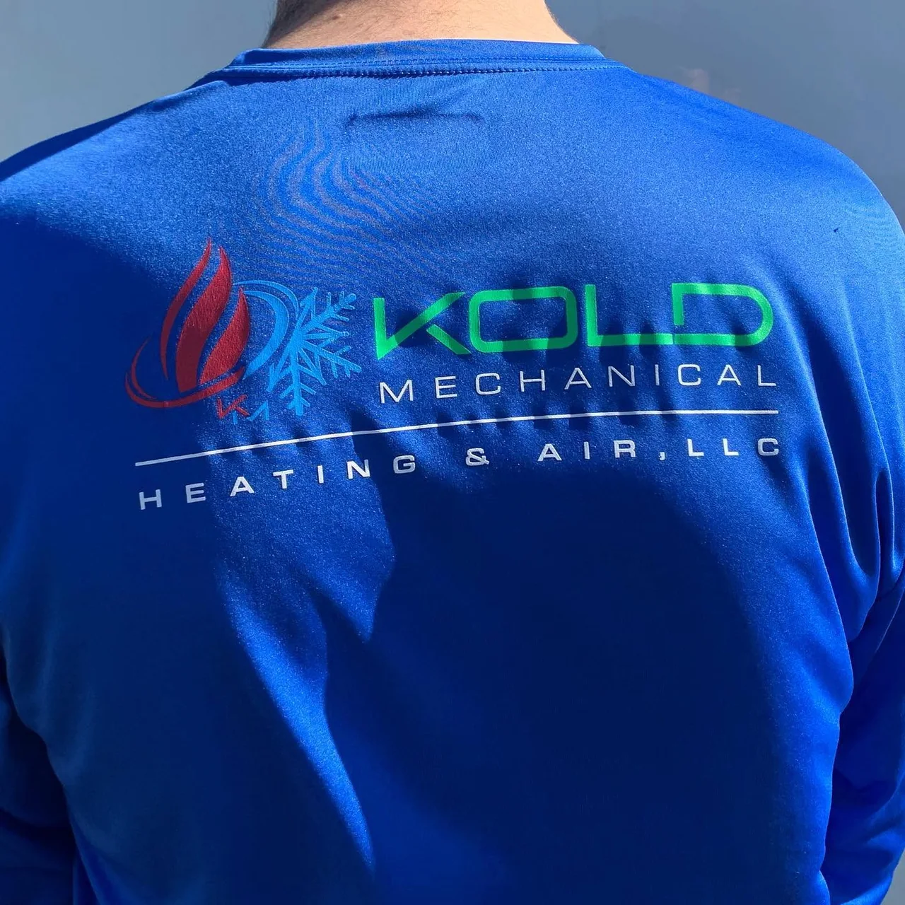 Close view of the KOLD Mechanical logo embroidered on a blue work shirt.